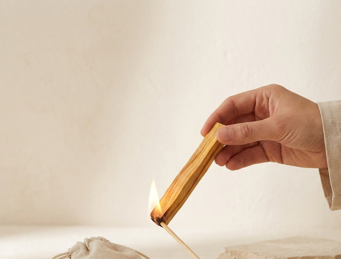 Palo Santo Holz wird mit einem Streichholz angezündet – Hand hält den Stick schräg nach unten, kleine Flamme am unteren Ende sichtbar