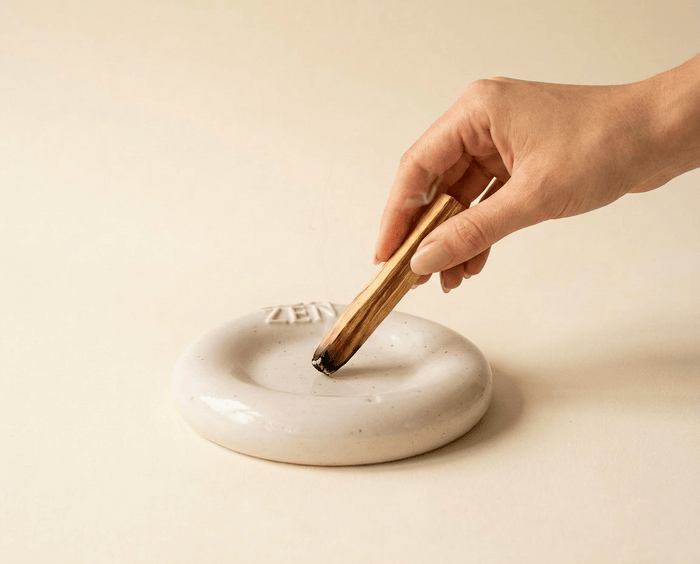 Palo Santo Holz wird in einer ZoaZen Keramikschale sicher ausgedrückt – Hand drückt den Stick mit der verkohlten Spitze in die Schale