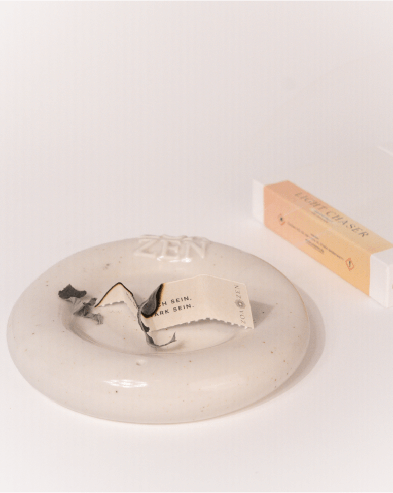 Verbranntes ZoaZen Räucherpapier mit Affirmation auf Keramik-Räucherschale – Light Chaser Collection im Hintergrund