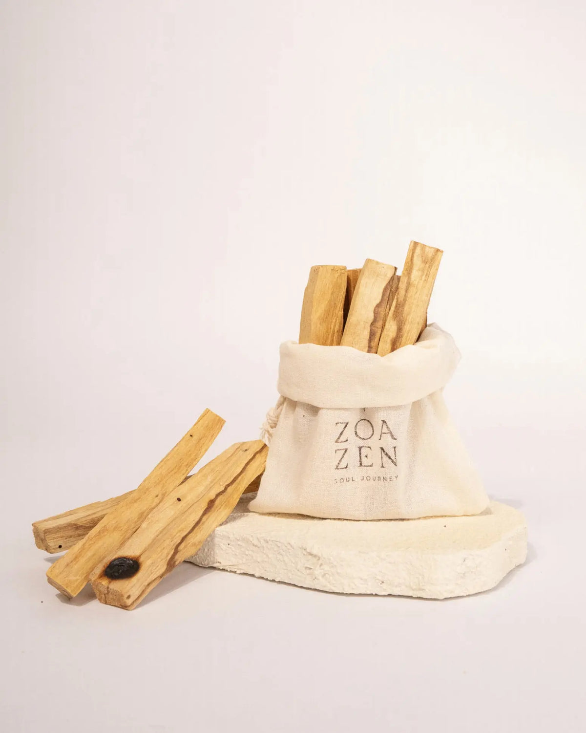 Palo Santo Holz Sticks neben ZoaZen Baumwollbeutel auf Natursteinplatte – Premium Räucherholz mit sichtbarer Harzmaserung
